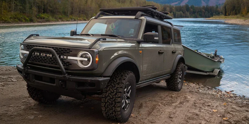 A dark green 2026 Ford Bronco Backing a boat in to a body of water.